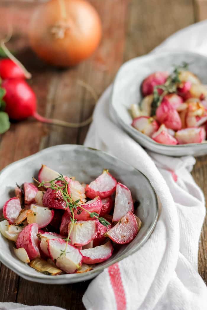 Photo shows two bowls of roasted radishes on a table 