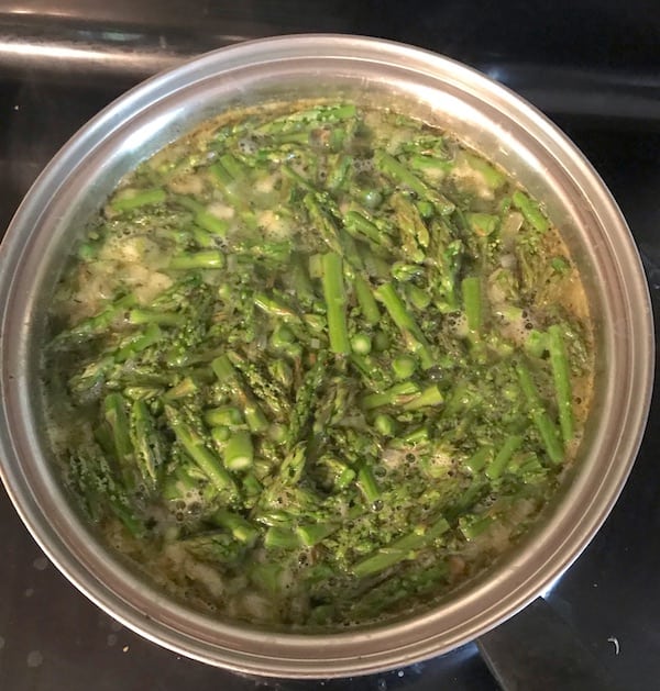 Image shows a large pan boiling asparagus on the stove
