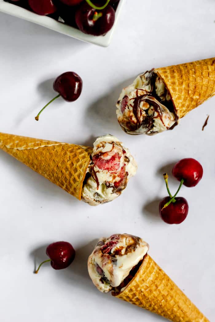 Photo shows several ice cream cones with cherry chocolate ice cream on a table