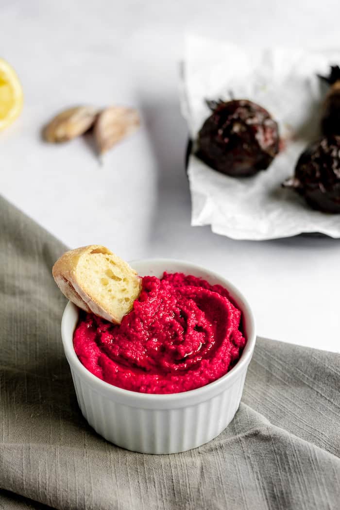 Image shows a small bowl of roasted beet hummus with a piece of bread in it