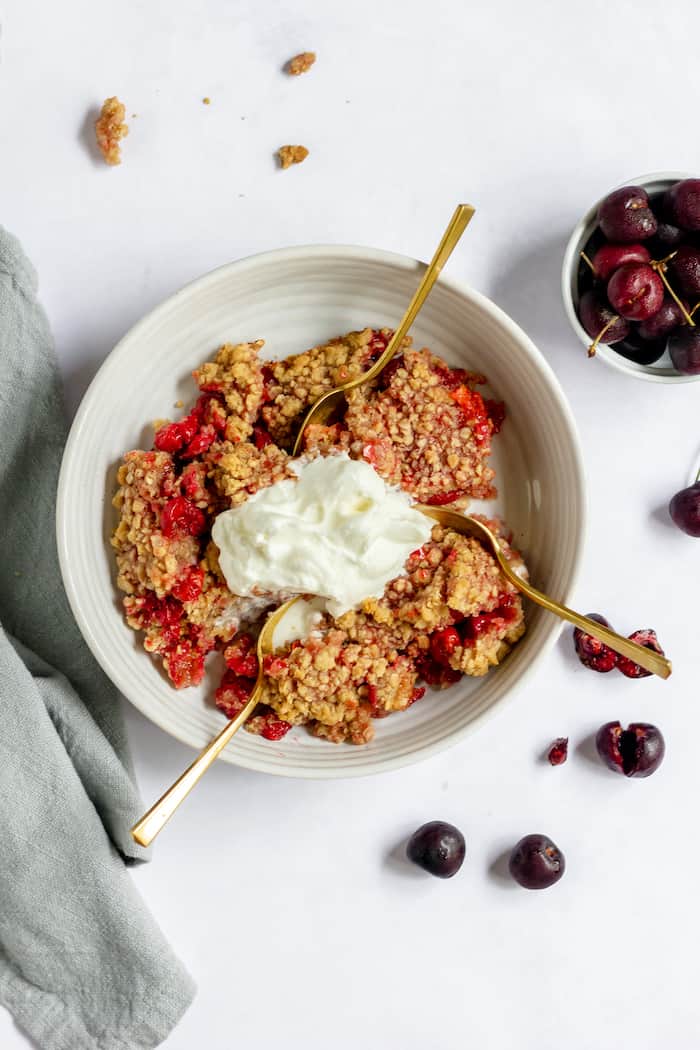 Image shows a large bowl of cherry crumble with three spoons