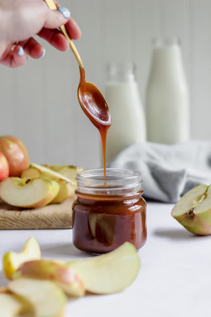 Photo shows a spoon drizzling homemade caramel sauce over a jar
