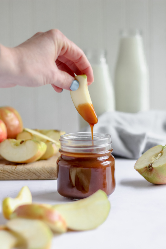 Photo shows a hand dipping an apple slice into a jar of caramel sauce