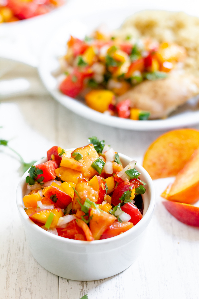 Photo shows a bowl of salsa with peaches and tomatoes in front of a plate of chicken with salsa