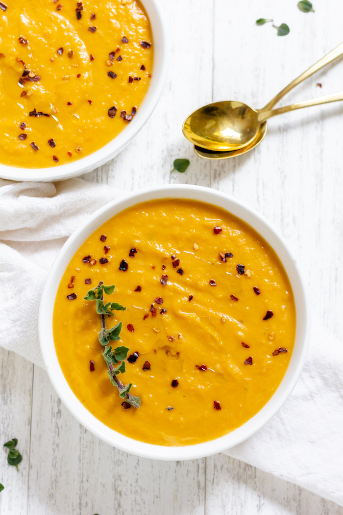 Image shows two bowls of butternut squash soup photographed from above with two spoons on a table