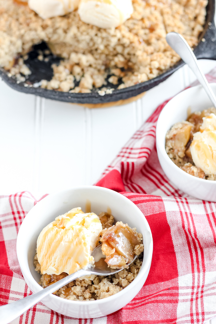 Image shows two bowls of apple crisp with ice cream next to a pan of apple crisp