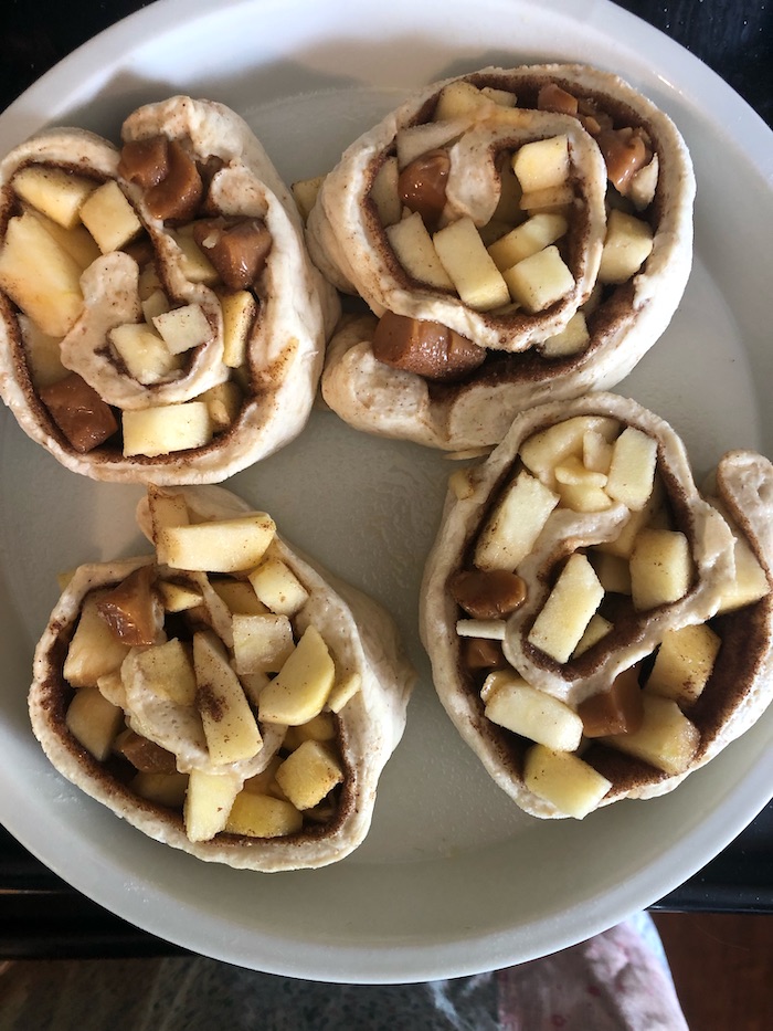 Photo shows four apple cinnamon rolls on a plate before baking 