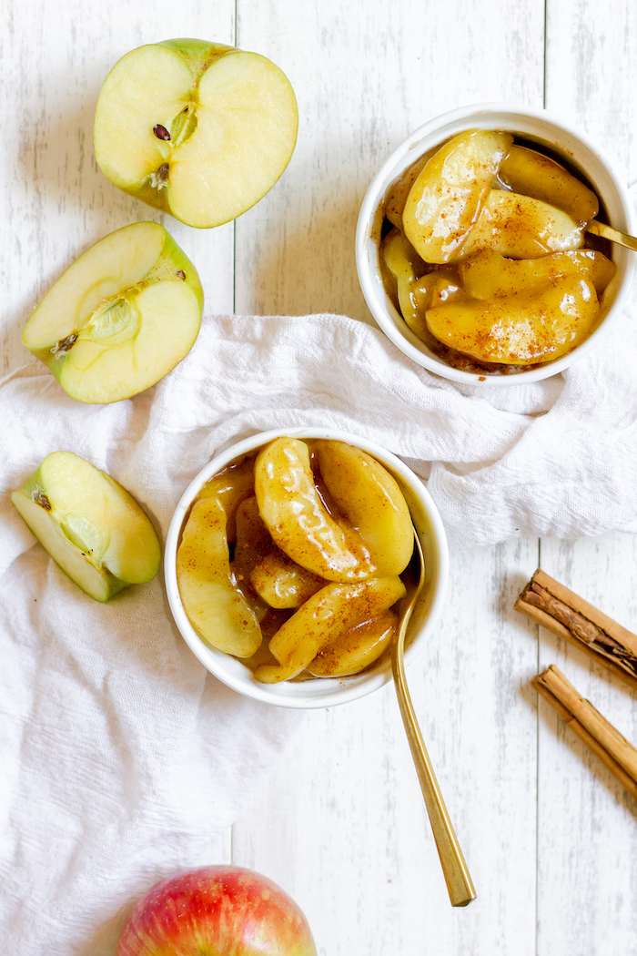 Image shows two bowls of fried apples, next to two apple halves