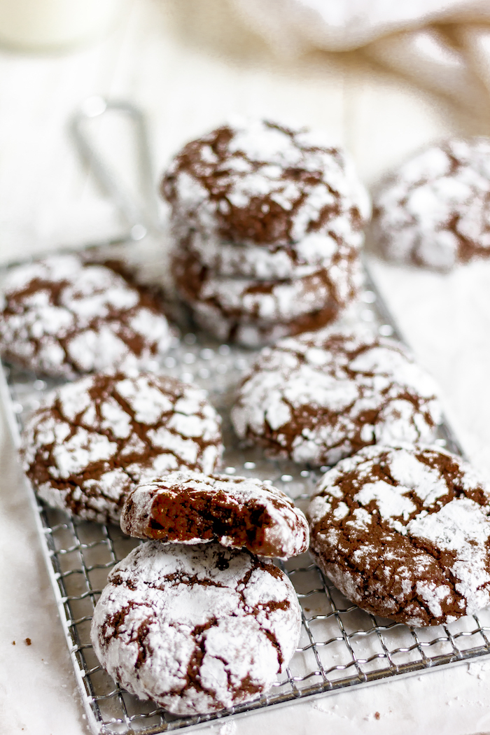 Image shows a close up of several chocolate crinkle cookies, one with a bite taken out of it