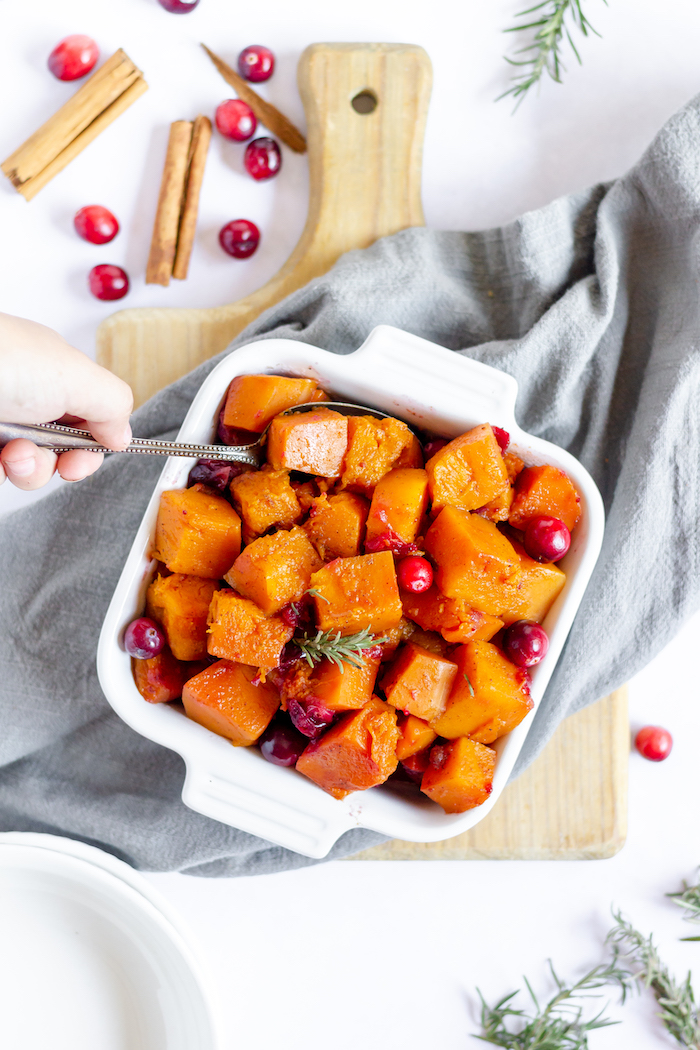Image shows a hand scooping butternut squash and cranberry from a white dish
