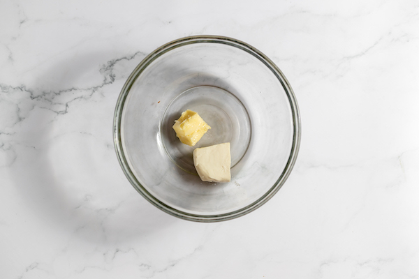 Image shows a glass bowl on a counter top, with cream cheese and butter in it