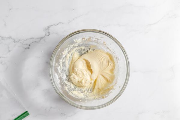 Image shows a glass mixing bowl with cream cheese and butter mixed together to make frosting