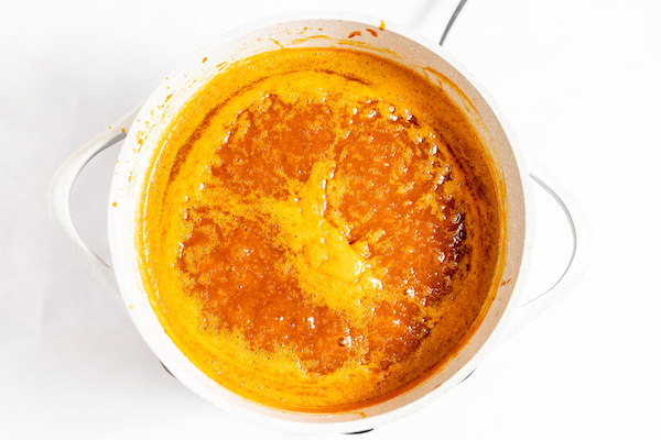 Image, taken from above, shows a white pot of pumpkin jam, boiling on the stovetop.