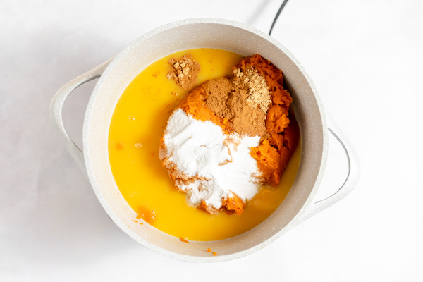 Image, taken from above, shows a white pot with the orange juice, pumpkin puree and spices poured into it. 